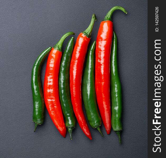 Green and red chili peppers on black background top view. Hot spicy food.