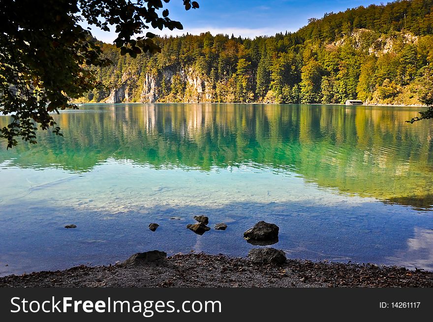 View from the shore to a beautiful alpine mountain lake surrounded by trees