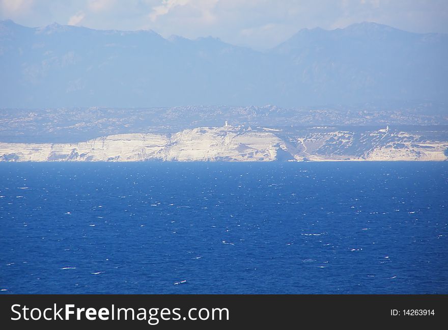 Straits of Bonifacio (Bocche di Bonifacio), strait between Sardinia (Italy) and Corsica (France) which divides the Tyrrhenian Sea from western Mediterranean Sea, and view of Bonifacio cliffs and mountains in the background. Straits of Bonifacio (Bocche di Bonifacio), strait between Sardinia (Italy) and Corsica (France) which divides the Tyrrhenian Sea from western Mediterranean Sea, and view of Bonifacio cliffs and mountains in the background