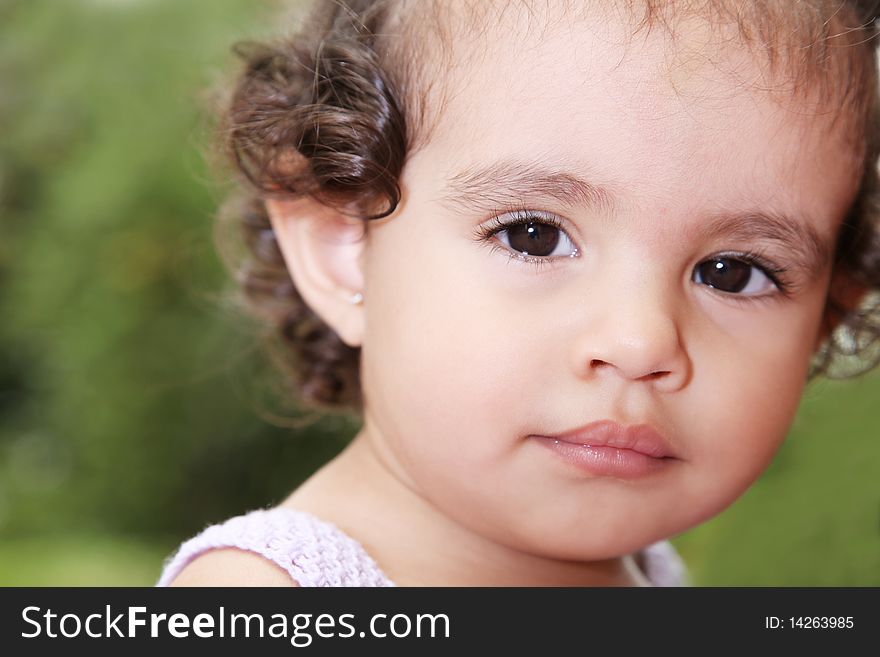 Beauty baby looking at camera over green background. Outdoor image