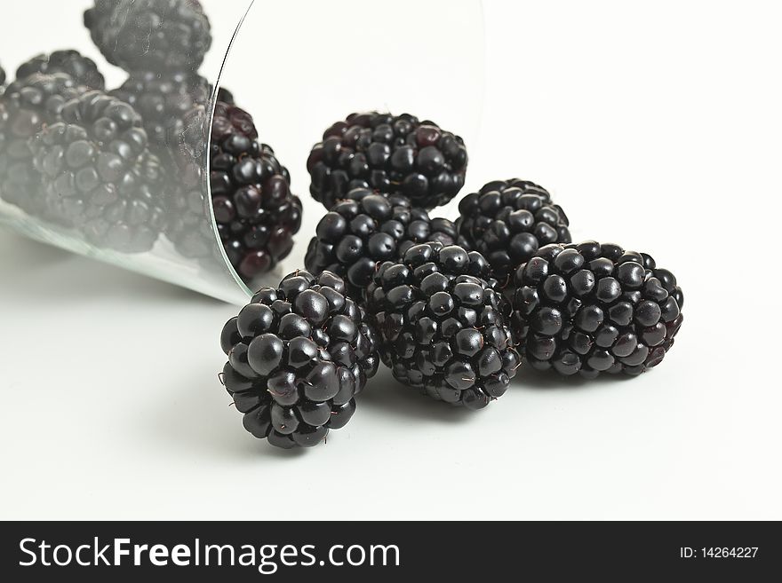 Blackberries in and out of a tipped on it's side glass with an isolated background. Blackberries in and out of a tipped on it's side glass with an isolated background