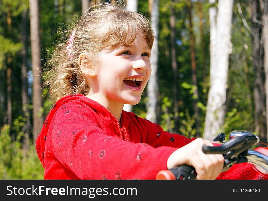 The joyful girl goes on a bicycle in the summer in park. The joyful girl goes on a bicycle in the summer in park