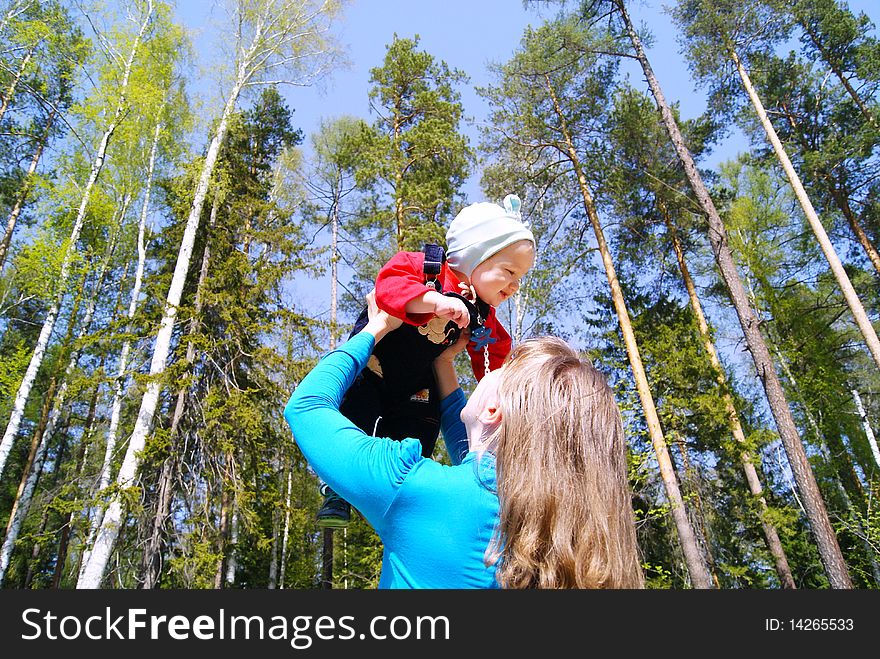 The girl lifts the kid up against trees in park in the summer. The girl lifts the kid up against trees in park in the summer
