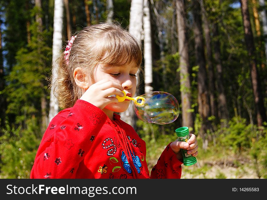 In the summer in park the girl in red clothes inflates a soap bubble. In the summer in park the girl in red clothes inflates a soap bubble