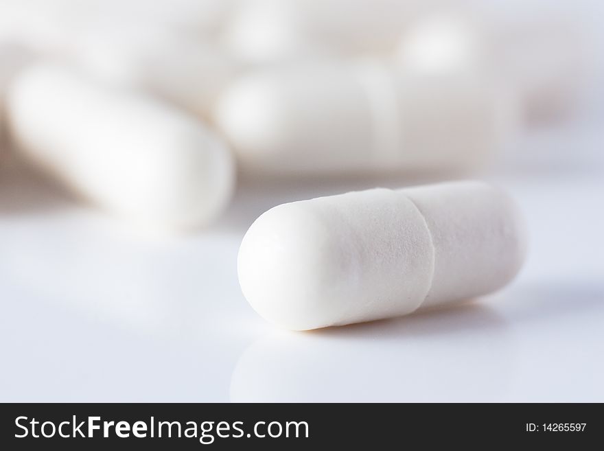 Macro shot of white capsuled pill and a heap of same pills defocused on background