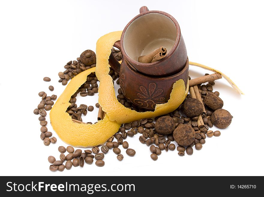 Two coffee cups, facing one another with sticks of cinnamon in the top cup with lying next to a yellow grapefruit peel, coffee beans and chocolate truffles. Two coffee cups, facing one another with sticks of cinnamon in the top cup with lying next to a yellow grapefruit peel, coffee beans and chocolate truffles