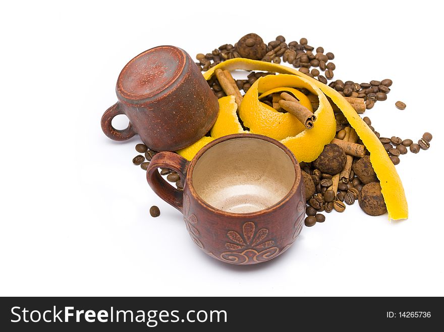 Two coffee cups, one of them turned, near the yellow peel of grapefruit lying on a pile of coffee beans, chocolate truffles and cinnamon sticks. Two coffee cups, one of them turned, near the yellow peel of grapefruit lying on a pile of coffee beans, chocolate truffles and cinnamon sticks