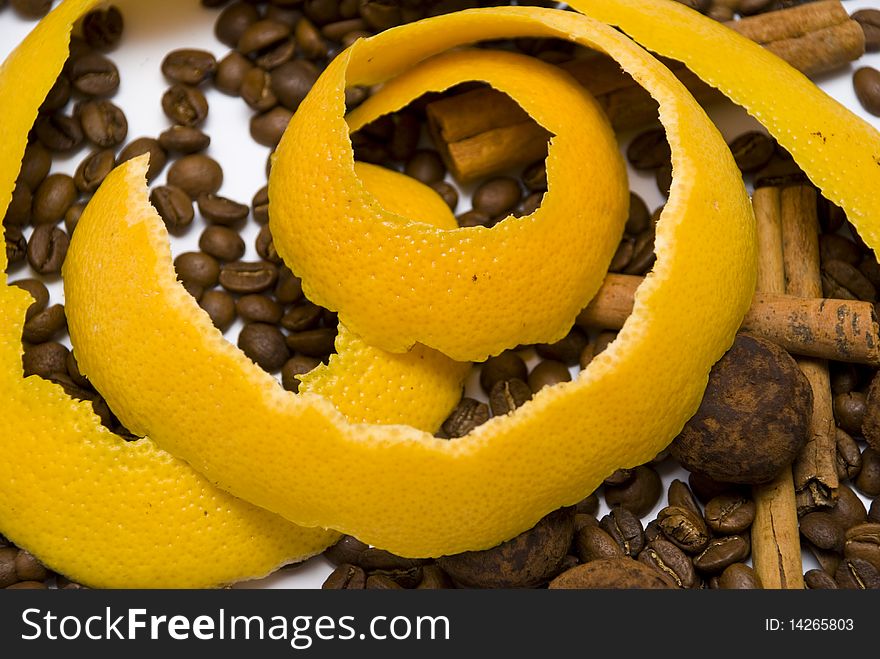 Yellow peel, spiral sliced, in coffee beans and cinnamon sticks and chocolate truffles on the white ground. Yellow peel, spiral sliced, in coffee beans and cinnamon sticks and chocolate truffles on the white ground