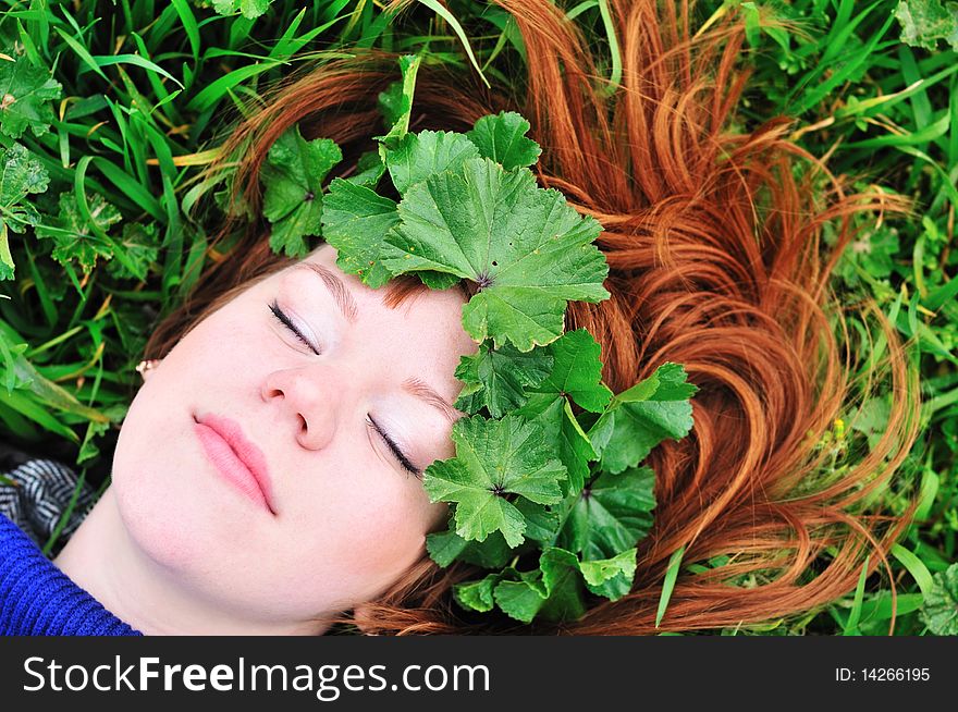 Redheaded girl laying on the green grass with crown from leaves. Redheaded girl laying on the green grass with crown from leaves