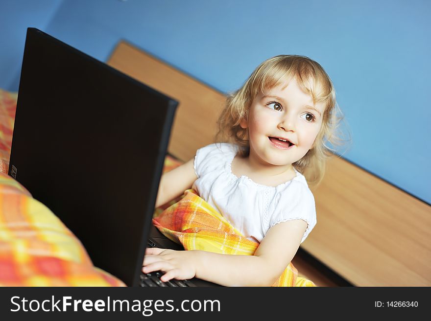 Cheerful little girl with laptop sits on bed of parents