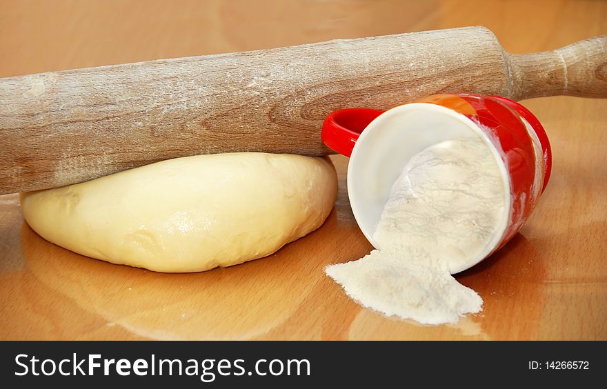 Rolling pin over dough and cup with flour on table in kitchen