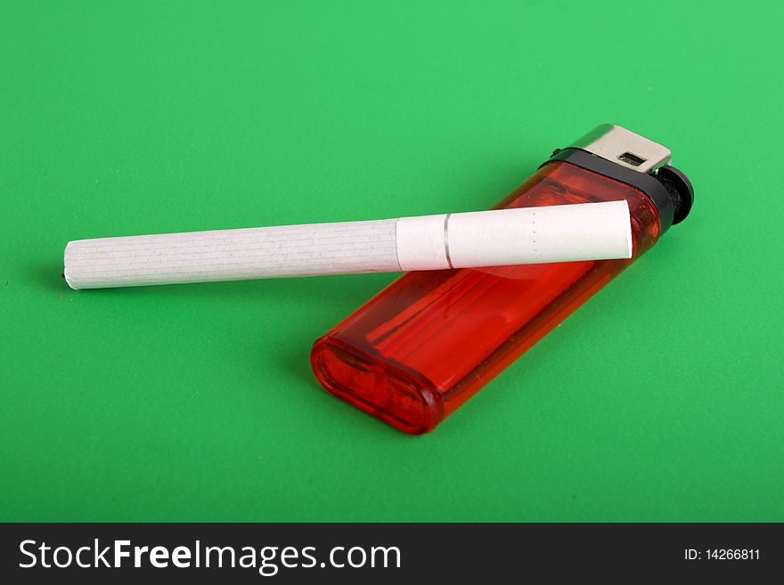 One cigarette with red lighter on green background. One cigarette with red lighter on green background