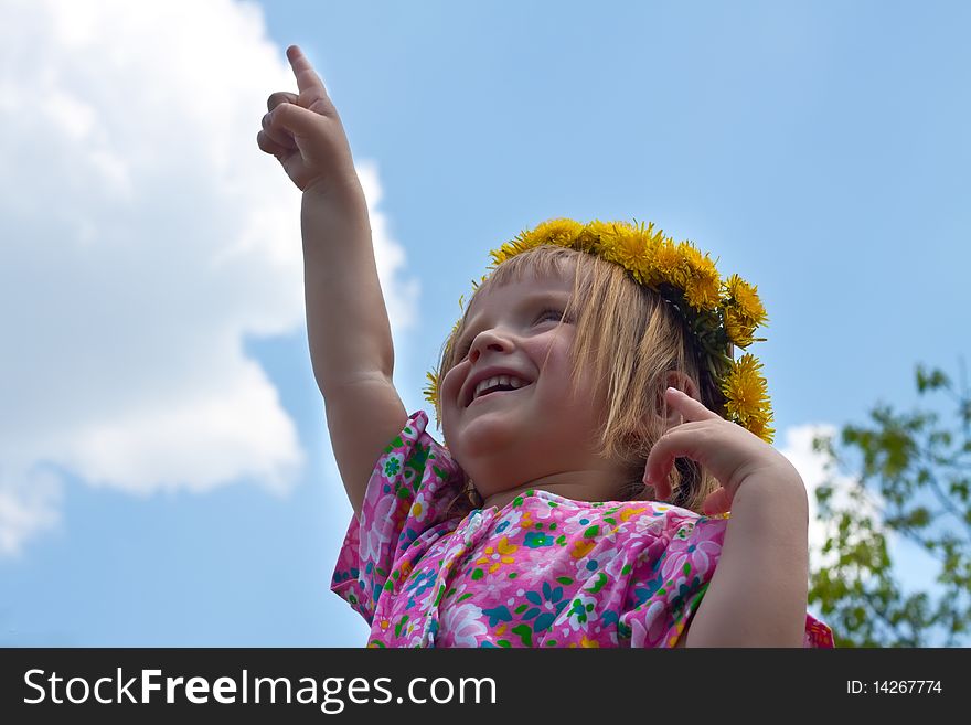 Portrait of little girl in dandelion crown pointing upwards