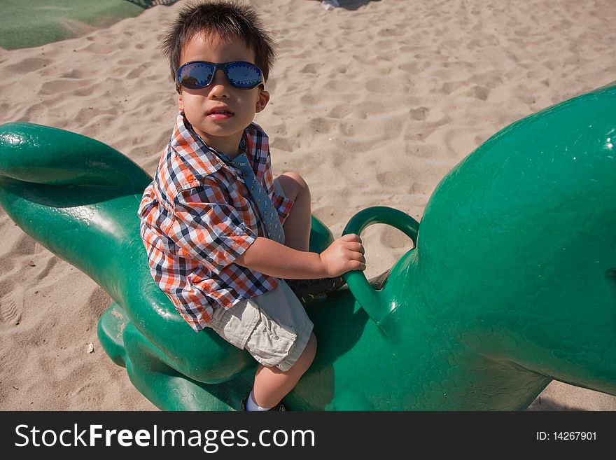 A cute boy is riding a toy dragon in a playground. A cute boy is riding a toy dragon in a playground