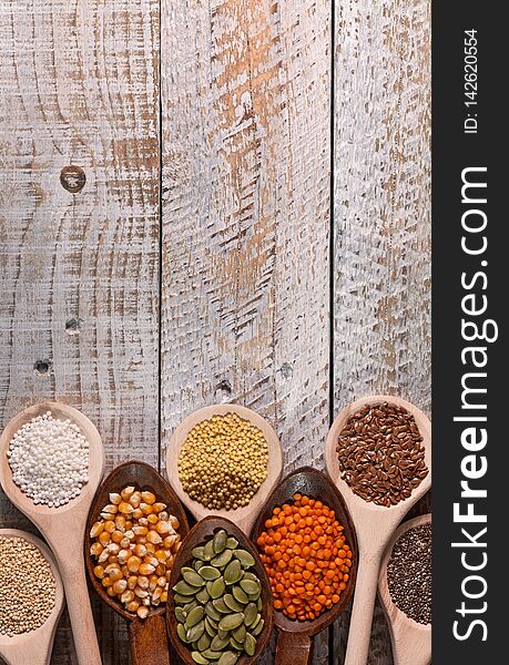 Various seeds and grains in wooden spoons on battered wooden surface - top view, close up, copy space