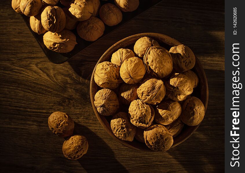 Walnuts lie in a bowl, next to them are scattered nuts on a wooden table. Walnuts lie in a bowl, next to them are scattered nuts on a wooden table