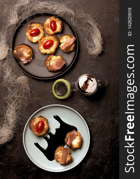 Vertical photo with top view on blue plate with puff pastry cups. Cups are stuffed by melted cheese. Ham and red tomatoes are on baked pastries. Dark sauce is spilled on plate. Vertical photo with top view on blue plate with puff pastry cups. Cups are stuffed by melted cheese. Ham and red tomatoes are on baked pastries. Dark sauce is spilled on plate