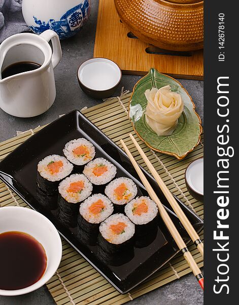 Japanese restaurant, sushi roll on black slate plate. Set for one person with chopsticks, ginger, soy, top view, copy