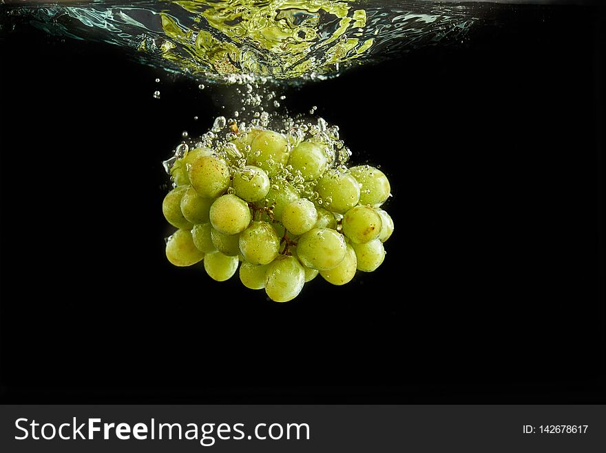 Fresh green grapes bunch splashing into water. Isolated on black background. Fresh green grapes bunch splashing into water. Isolated on black background