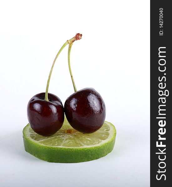 Cherries resting atop lime slice isolated. Cherries resting atop lime slice isolated