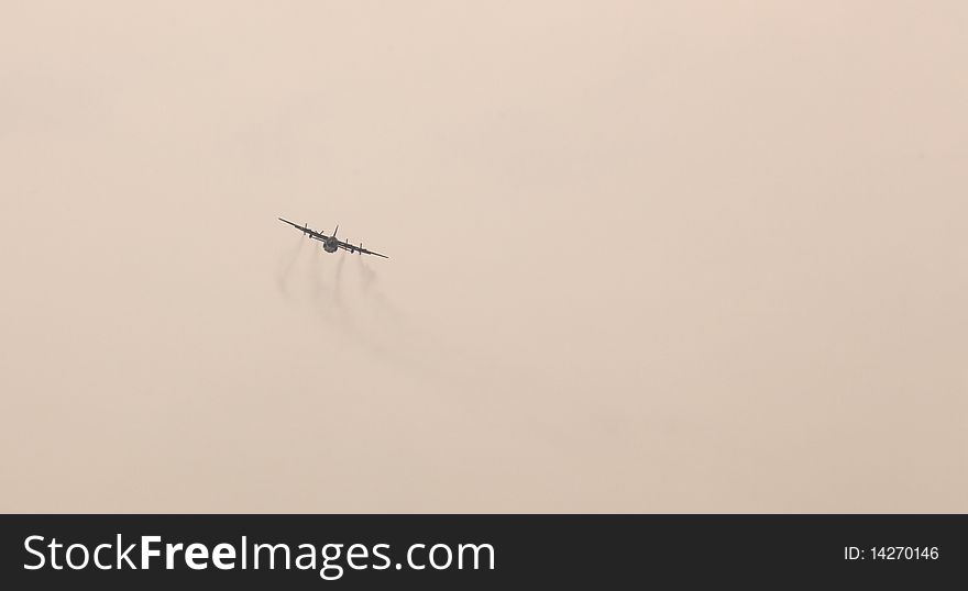 Front view silhouette of heavy military airplane with plume against hazy sky