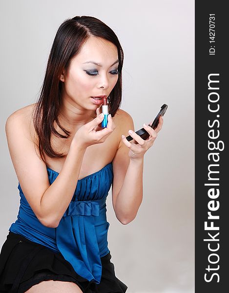 An Asian woman sitting on the floor in the studio and putting lipstick on her lips for the next photo shoot, for light gray background. An Asian woman sitting on the floor in the studio and putting lipstick on her lips for the next photo shoot, for light gray background.