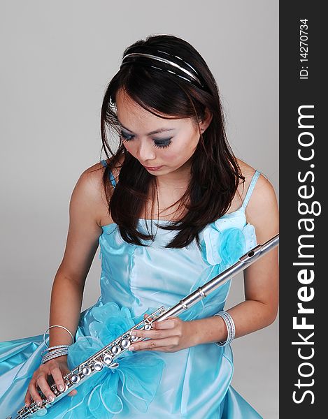 A young Asian woman in an light blue evening dress holding the flute standing in the studio for light gray background. A young Asian woman in an light blue evening dress holding the flute standing in the studio for light gray background.