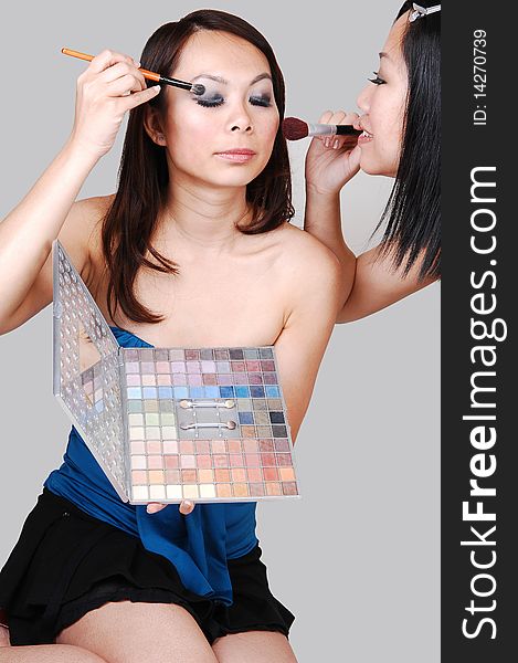 Two Asian woman kneeling on the floor in the studio and helping each other with the makeup for the next photo shoot, for light gray background. Two Asian woman kneeling on the floor in the studio and helping each other with the makeup for the next photo shoot, for light gray background.