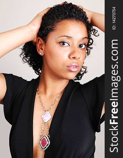 A beautiful Hispanic woman standing in the studio for a portrait with her black curly hair, in a black dress and nice necklace, light gray background. A beautiful Hispanic woman standing in the studio for a portrait with her black curly hair, in a black dress and nice necklace, light gray background.