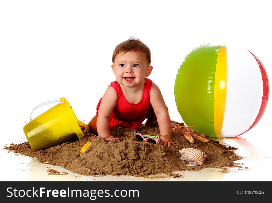 A happy baby girl crawling over a sand pile with beach toys, sunglasses and seashells nearby. A happy baby girl crawling over a sand pile with beach toys, sunglasses and seashells nearby.