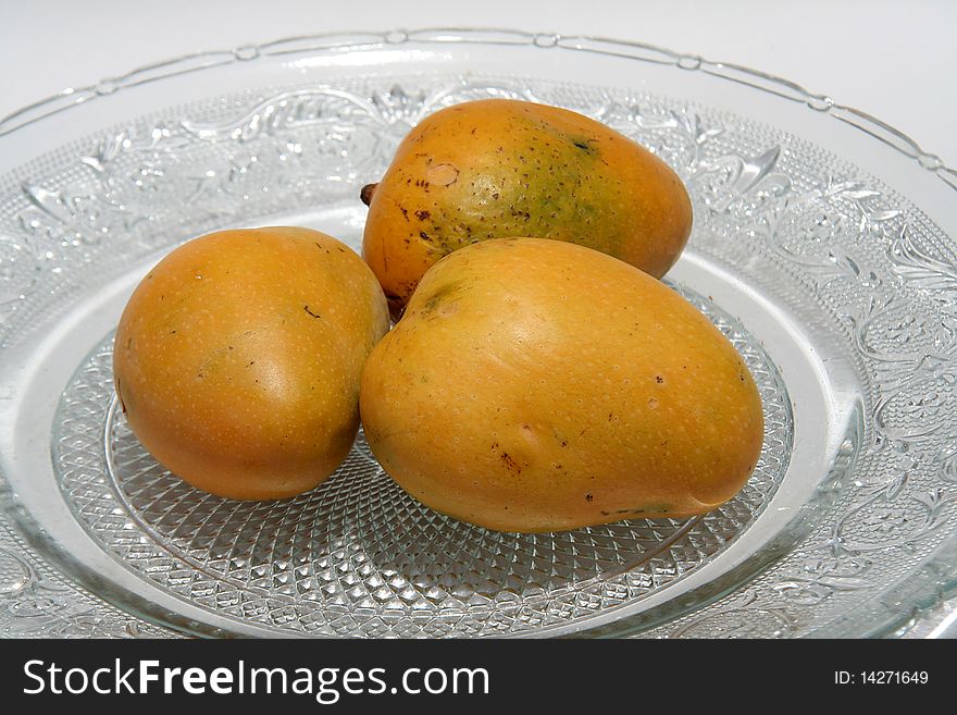 Golden yellow coloured, three ripe mangoes in glass tray