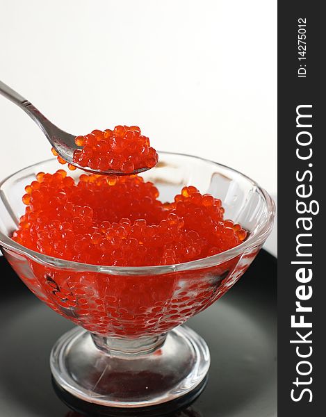 Red caviar in a glass vase on a black plate