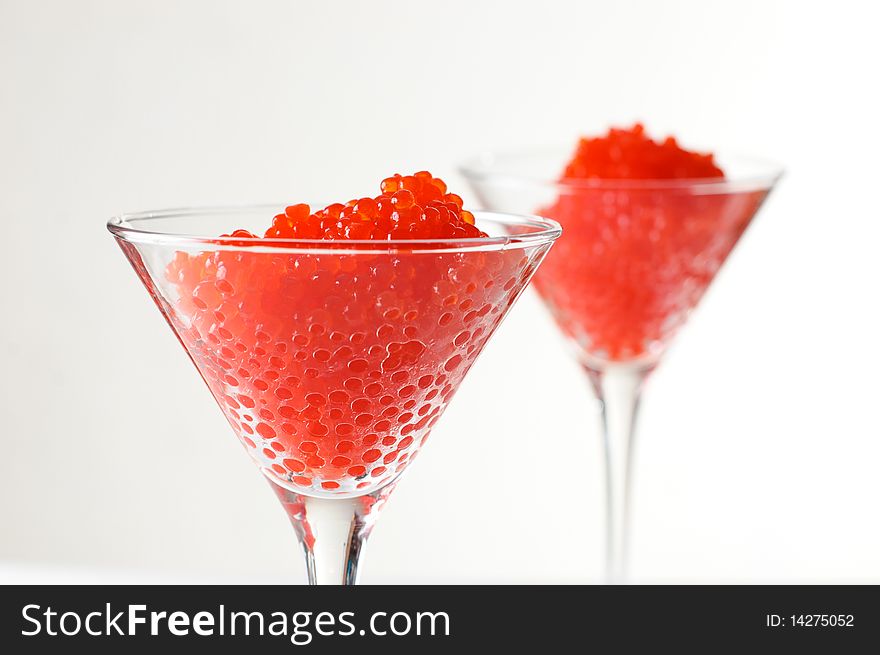 Two servings of red caviar in glass goblets on a white background