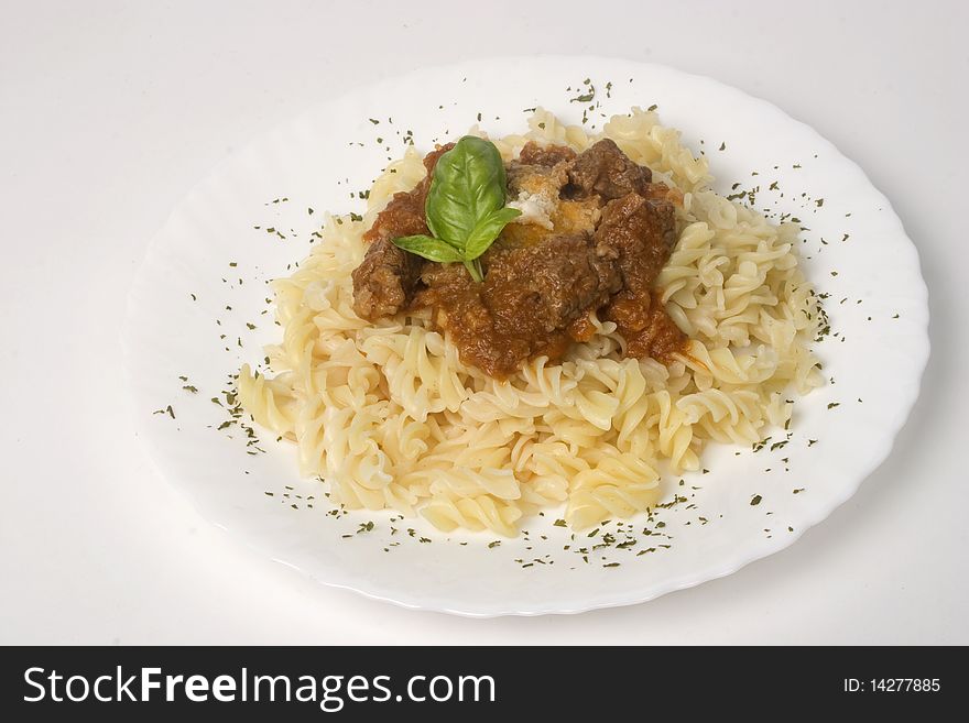 Fusilli with meat ragout, goulash, stewed beef on plate. Basil leaf and sheese on top. Isolated on white background.