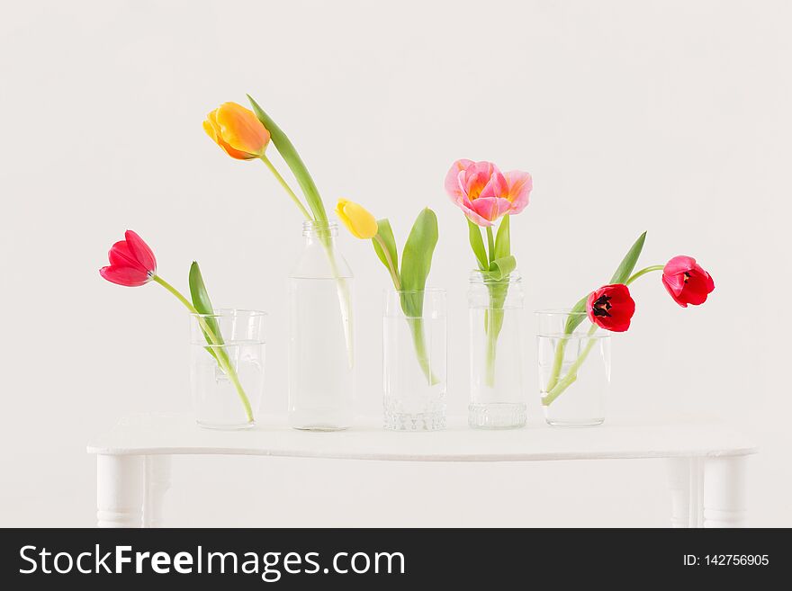 Tulips in glass bottles on white background