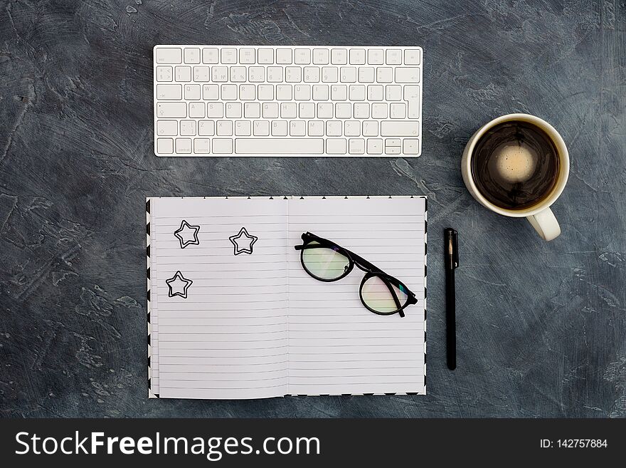 Work space. Office space. Black paper clips and pen on opened blank copybook, coffee, glasses on dark black abstract