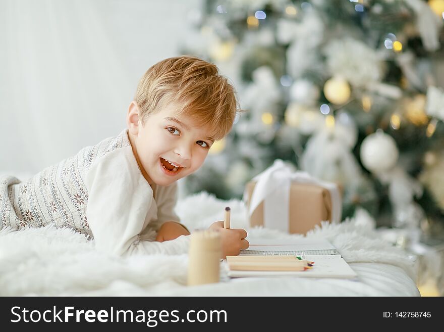 Beautiful little baby boy in pajamas with stars celebrates Christmas. New Year`s holidays. Toddler play in white Christmas sleigh in the festively decorated room, copy space on right area.