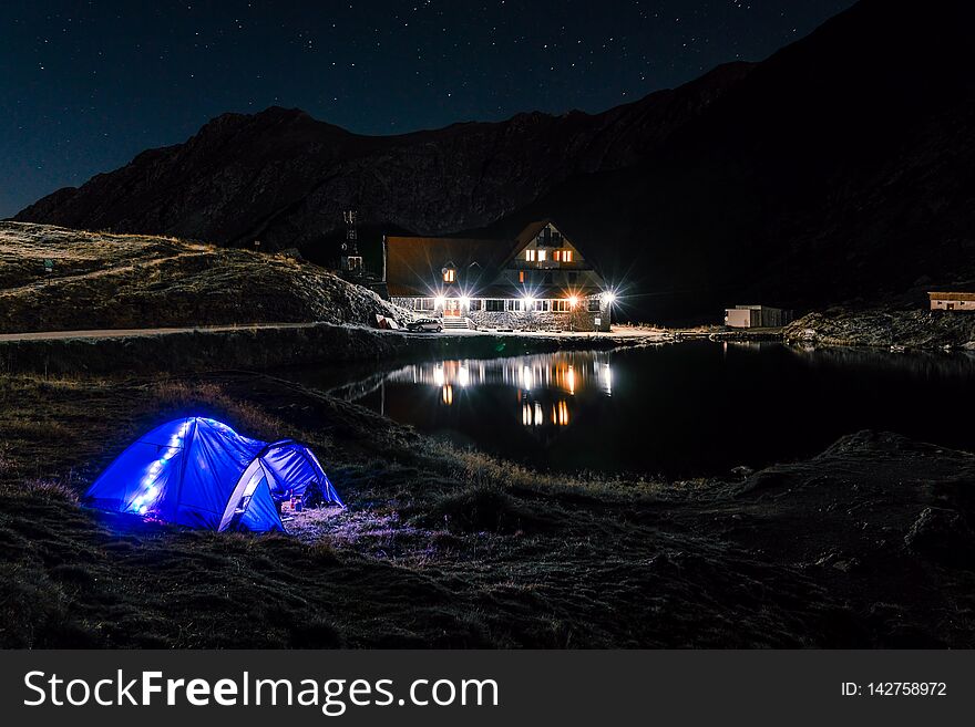 Night mountain landscape with illuminated blue tent. Mountain peaks and the moon. outdoor at Lacul Balea Lake, Transfagarasan