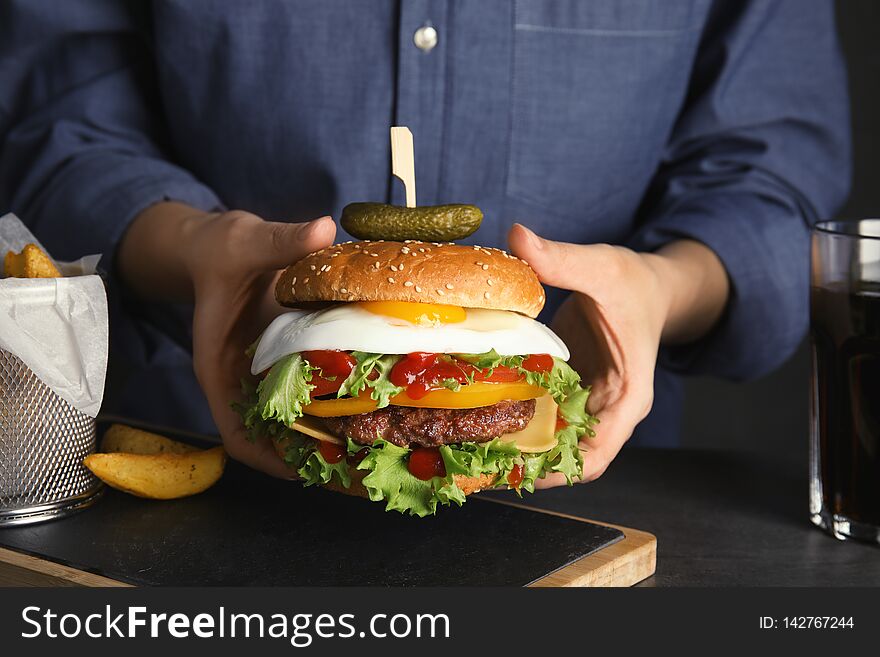 Woman holding tasty burger with fried egg over table, closeup