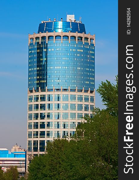 Modern business tower. Blue glass and concrete. Green trees in front of it.