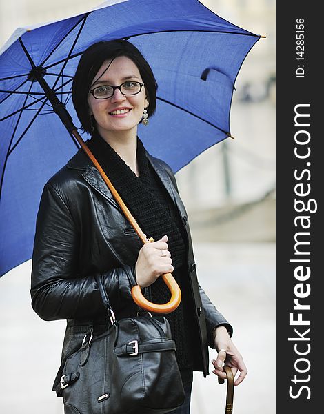 One young happy woman walking in cyti with rainy weater and blue umbrella. One young happy woman walking in cyti with rainy weater and blue umbrella