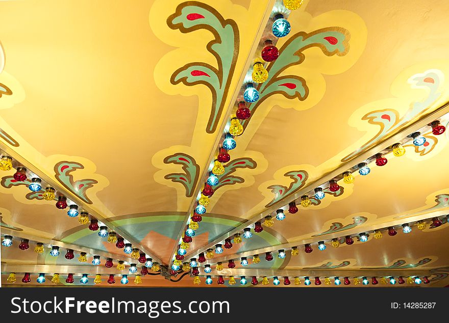 Decorative painted ceiling with radiating rows of colored lights at a fairground. Decorative painted ceiling with radiating rows of colored lights at a fairground.