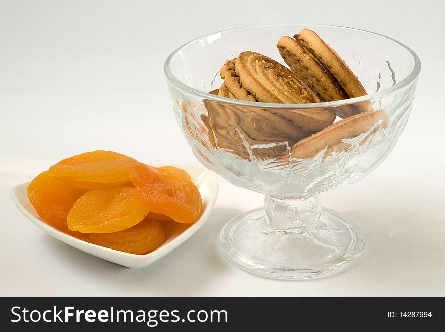 Dried apricots at white plate close-up and cookies in a vase on a white background. Dried apricots at white plate close-up and cookies in a vase on a white background