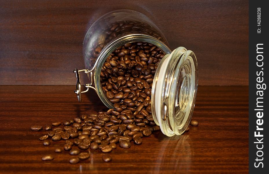 Coffee beans spilling out of a cristal jar in a wood background