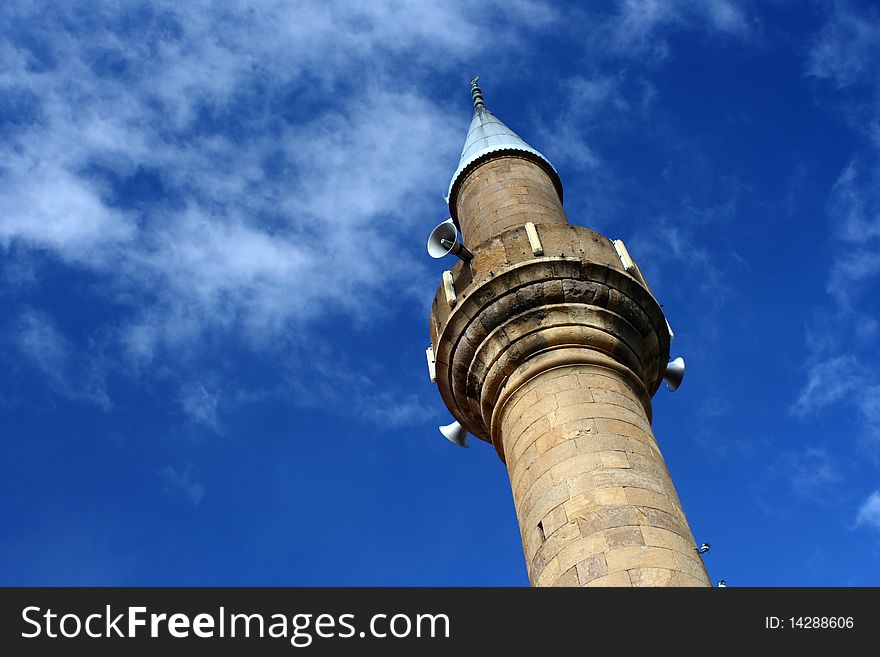 The minaret of a Turkish mosque shot at an angle against the blue sky. The minaret of a Turkish mosque shot at an angle against the blue sky