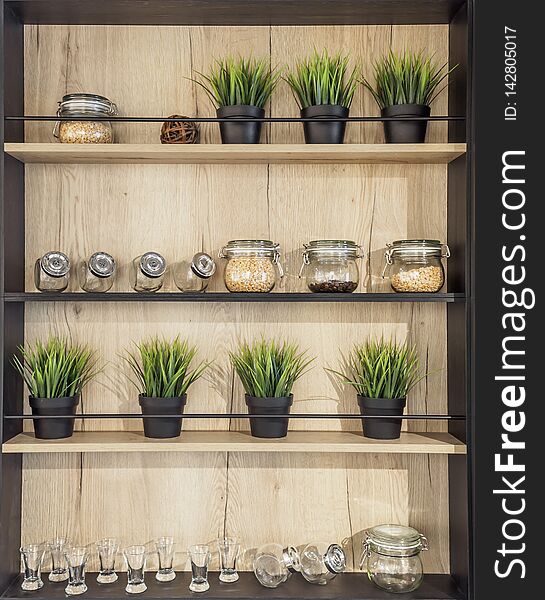 Wooden helf with kitchenware. Glass jars with spices pot plant glasses on the wooden rack kitchen background