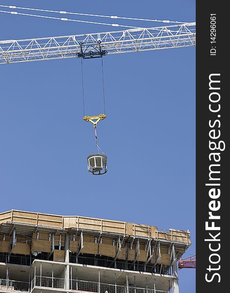 Crane working on an Unfinished / under construction apartment building against a blue sky. Crane working on an Unfinished / under construction apartment building against a blue sky