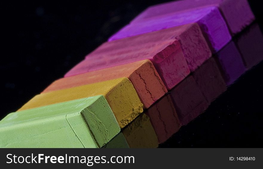 Colored chalk lined up at an angle on a black reflective background. Colored chalk lined up at an angle on a black reflective background