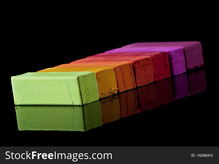Colored chalk lined up evenly on a black reflective background. Colored chalk lined up evenly on a black reflective background