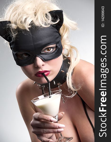 Portrait of the blond girl wearing black cat, licking - drinking milk from the martini glass. Portrait of the blond girl wearing black cat, licking - drinking milk from the martini glass